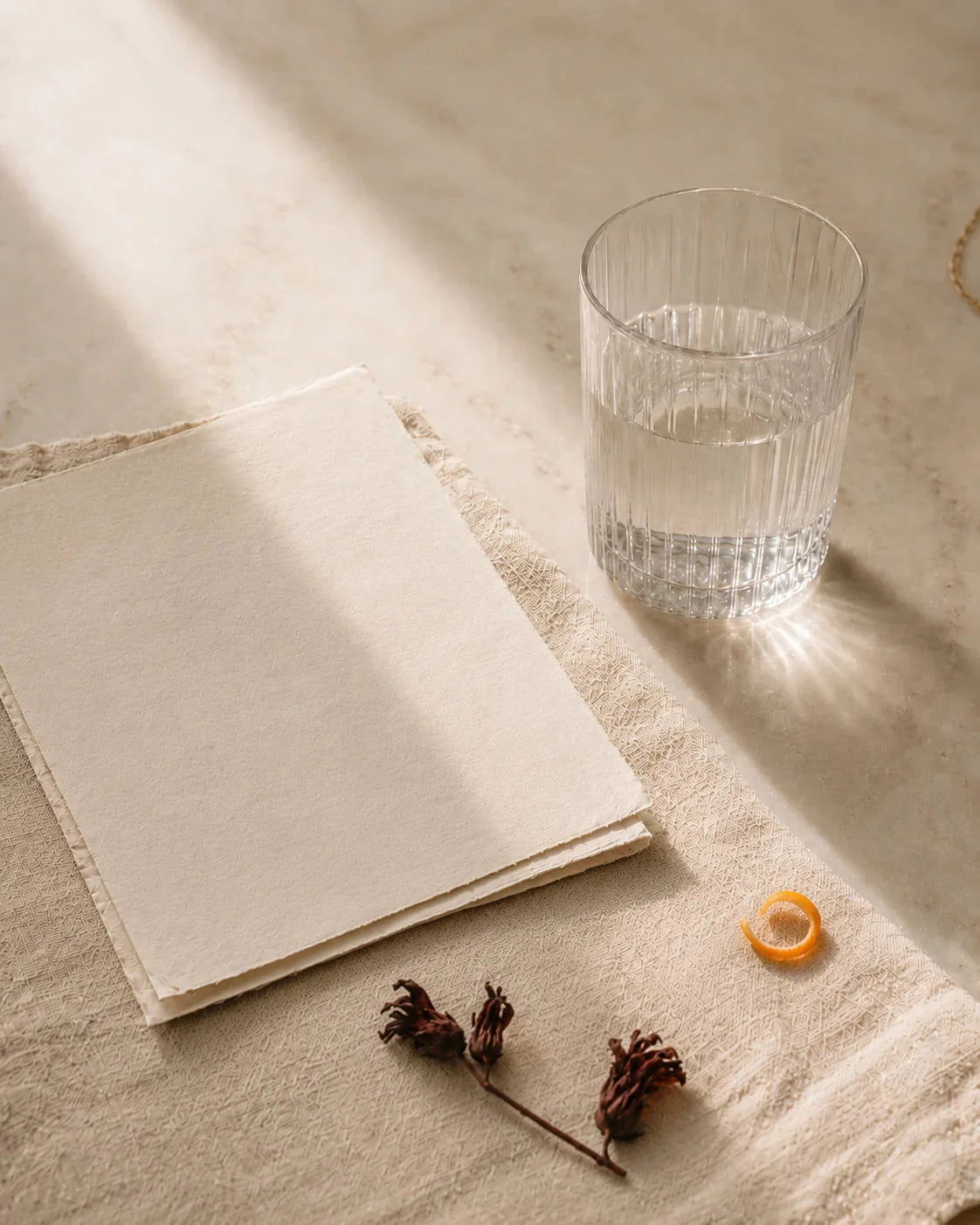A journal, a glass of water, dried hibiscus and citrus peel on linen