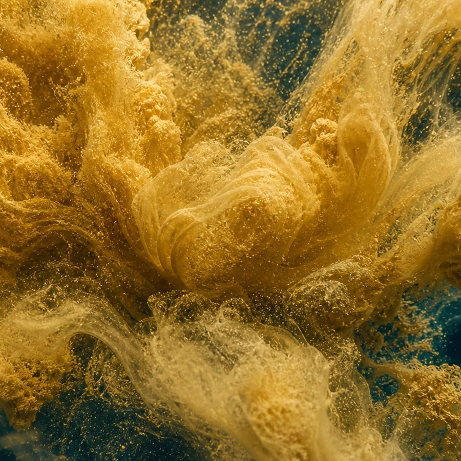 Golden powder blooming through water against deep teal